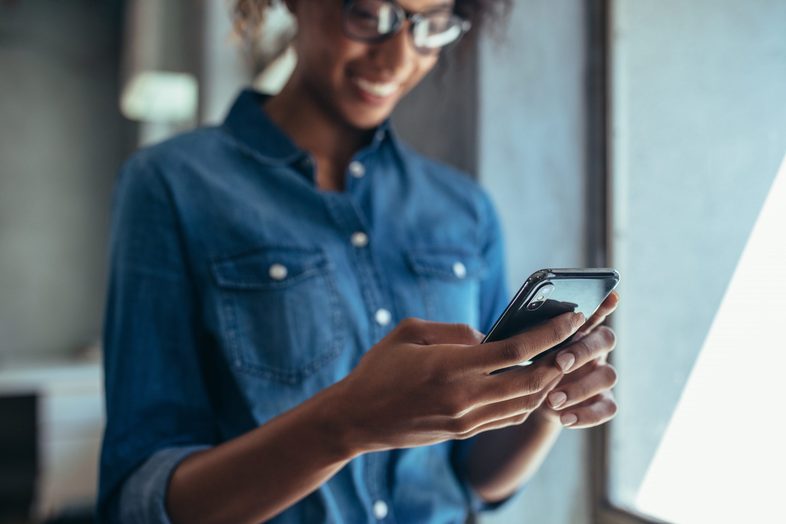 Businesswoman standing in office and using her mobile phone. Focus on smart phone in hand of a female wearing casuals.